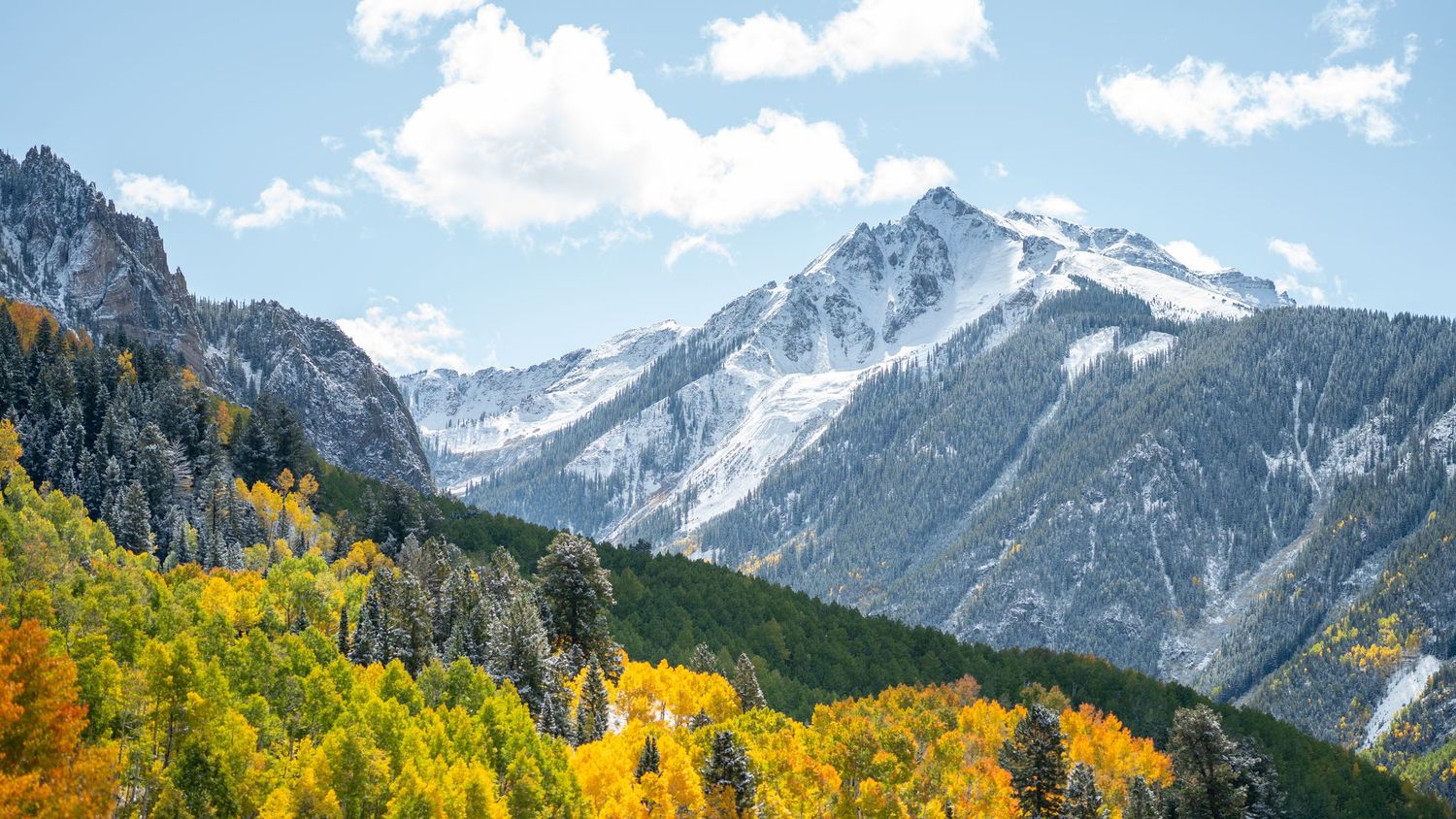 Mountain landscape with snow-covered peaks against bright blue sky and white clouds.