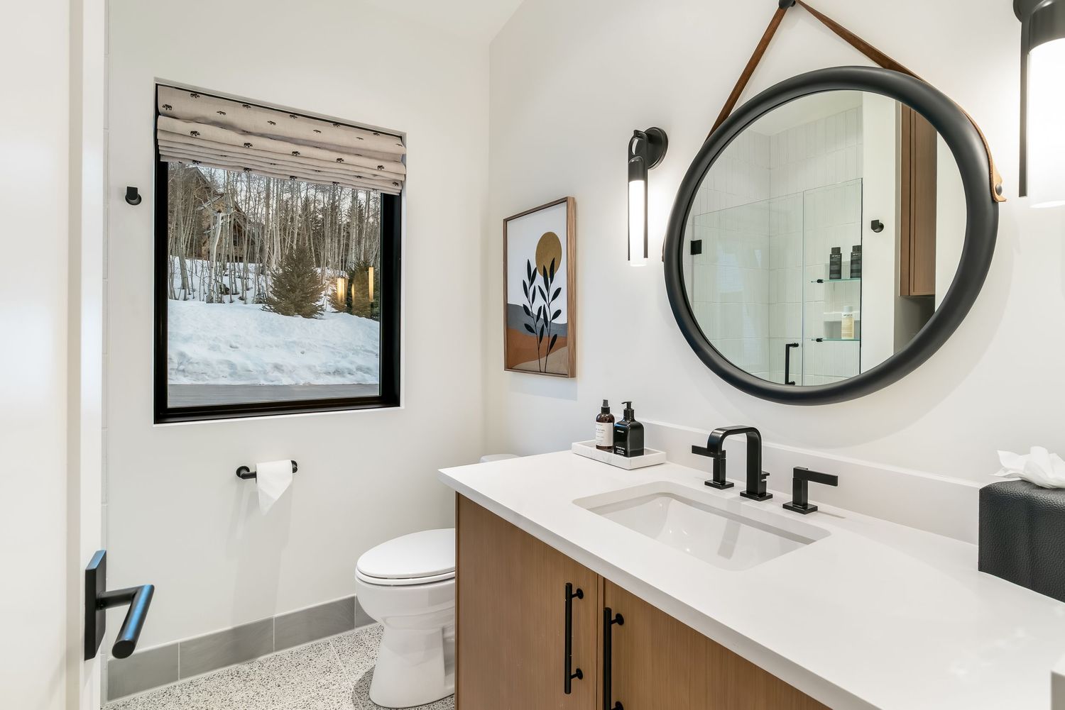 Modern white bathroom features a round black mirror, floating vanity, and sleek fixtures against marble-look walls.
