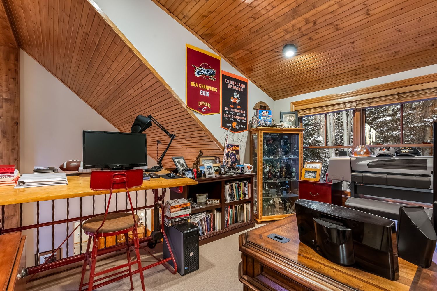 Open concept cabin interior with wood paneled ceiling, rustic decor, and entertainment area.