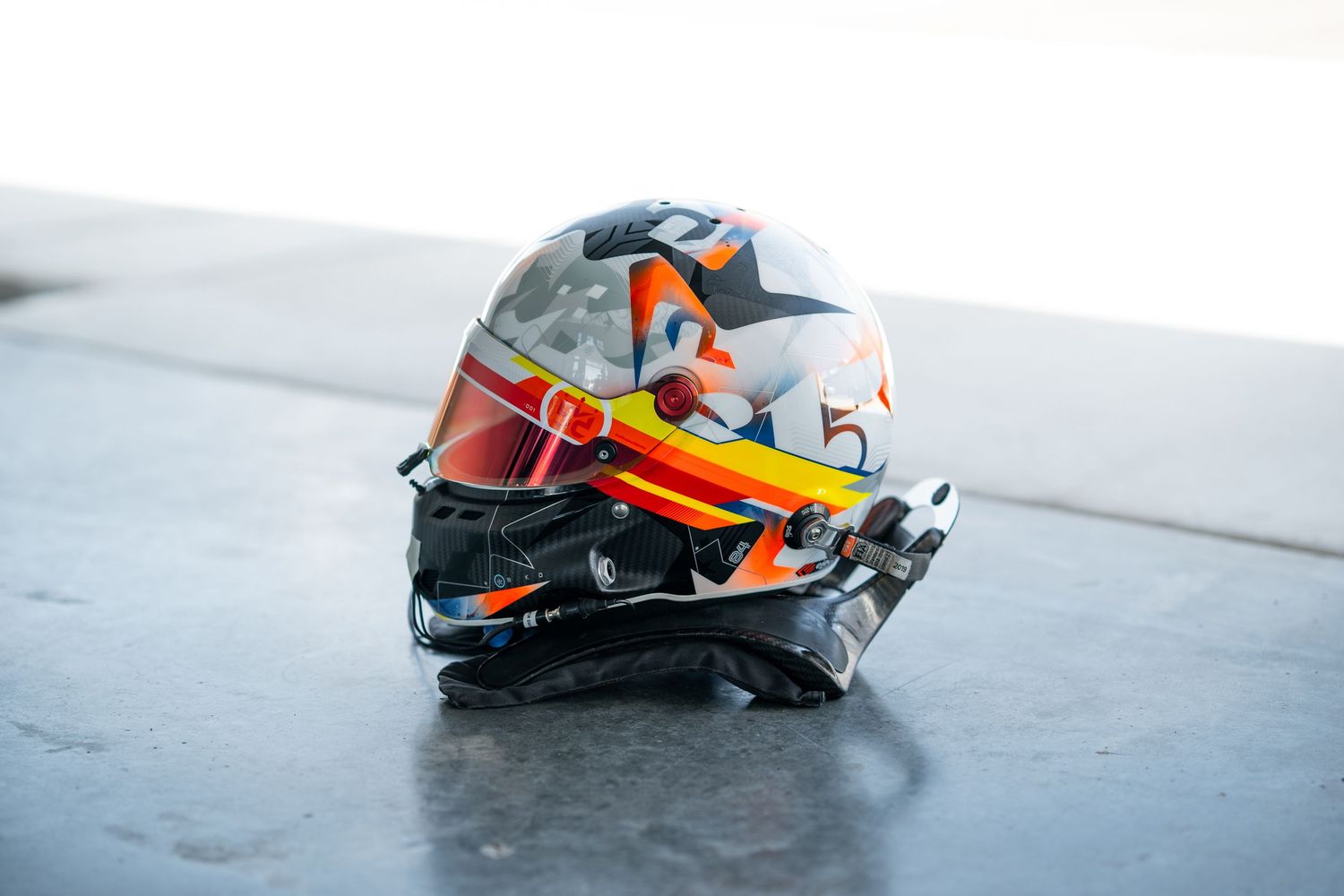 Professional racing helmets displayed on a light gray surface showcasing different sponsor logos.