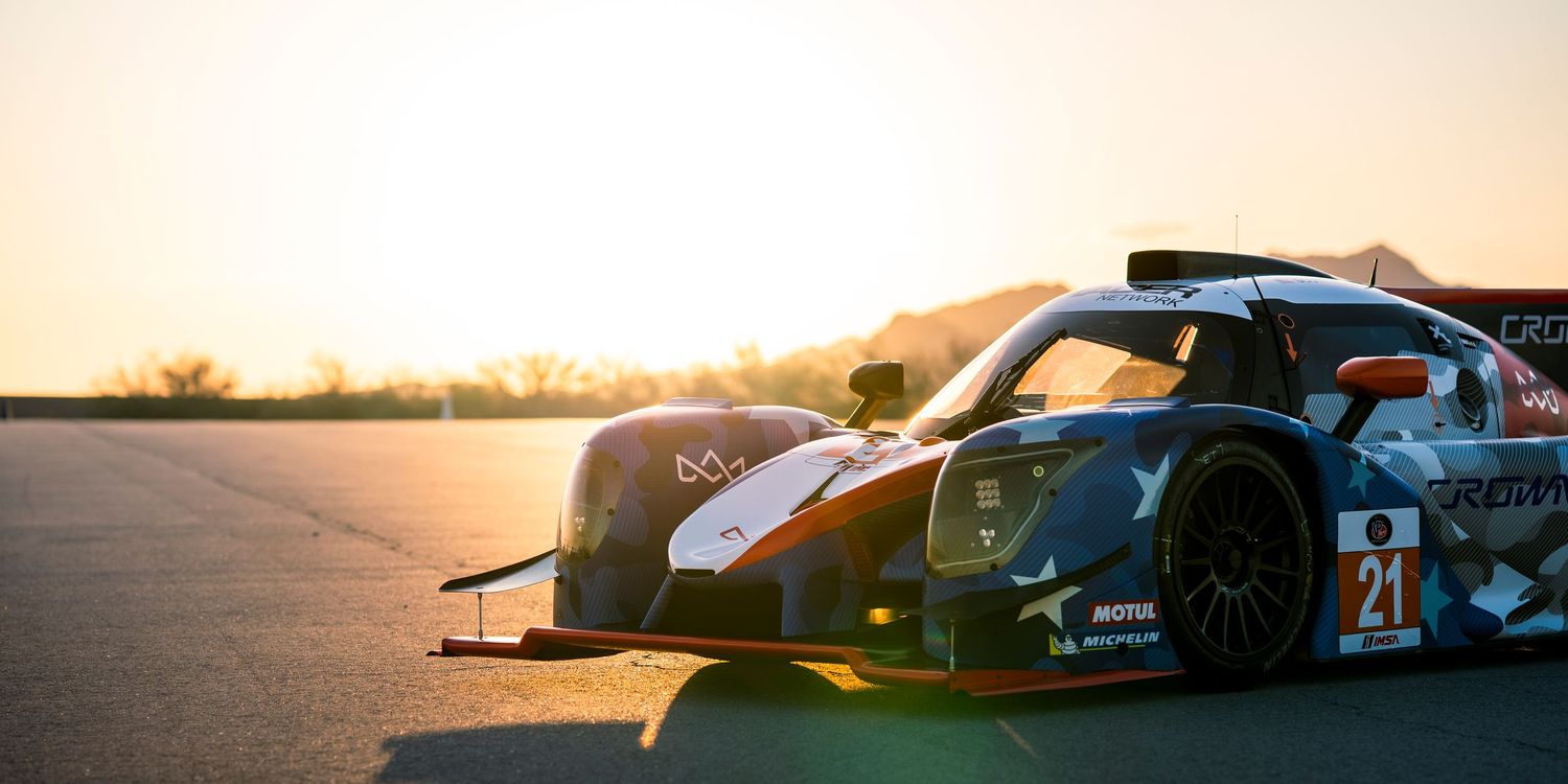 Silhouette of race cars against an orange sunset sky with mountain landscape.