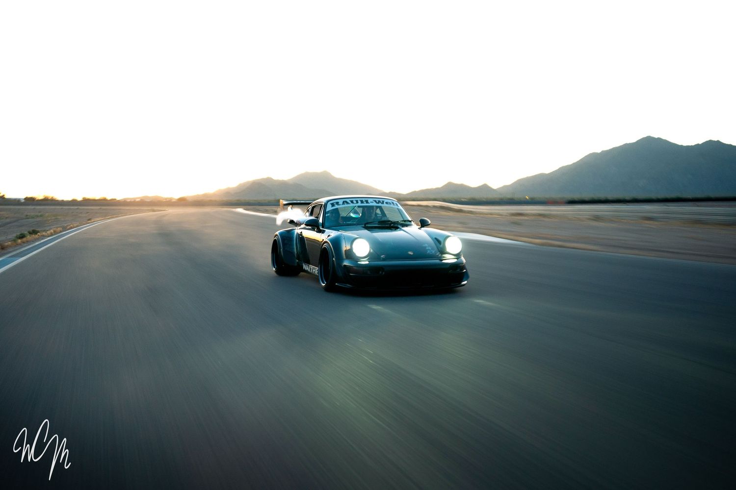 Modified Porsche 911 speeding on desert road at sunset with mountains in background.