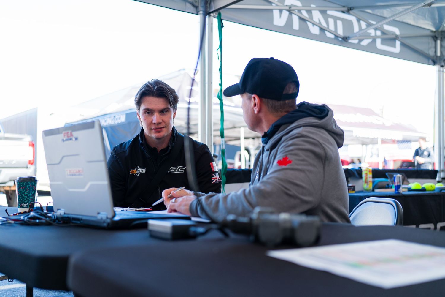 Racing team personnel working on laptops and analyzing data at a pit wall station.