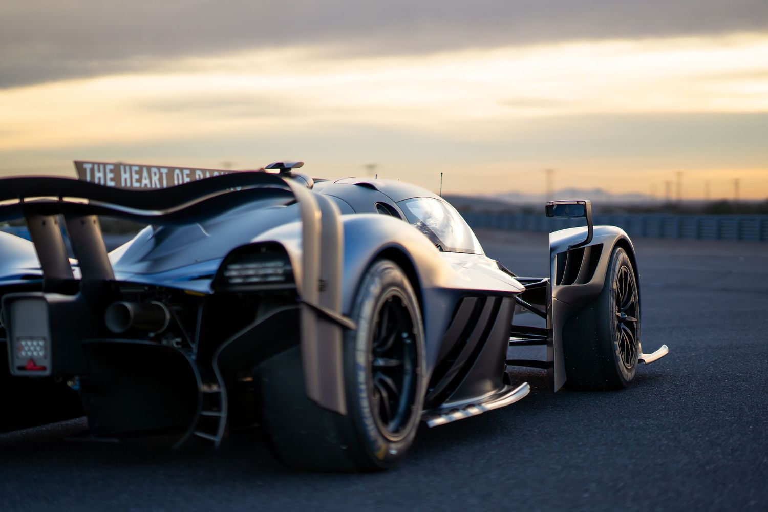 A sleek silver prototype race car with aerodynamic bodywork and large rear wing photographed at sunset.