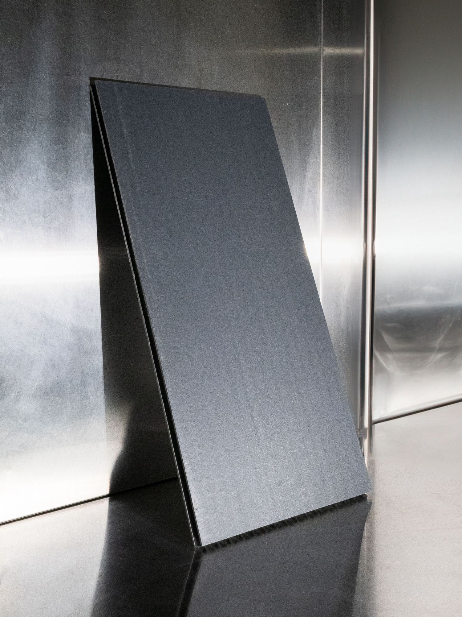 Sleek black panel standing at an angle against a metallic reflective surface creating dramatic shadows.