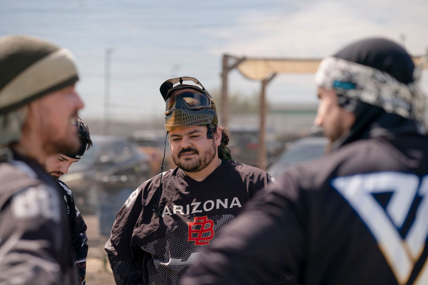 Team members gather for strategy discussion during paintball tournament.