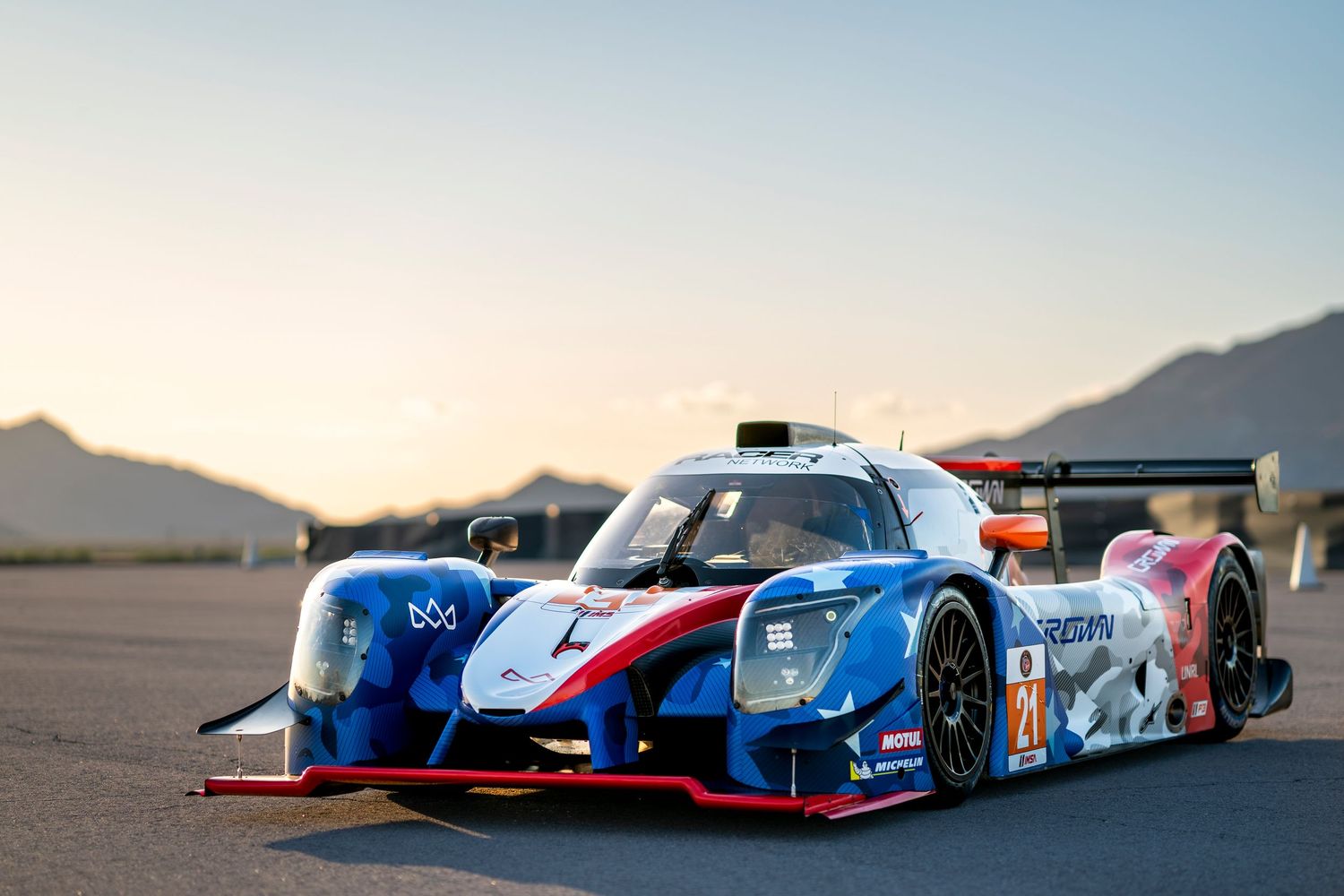 Race cars arranged on desert track with mountains silhouetted against bright sky.