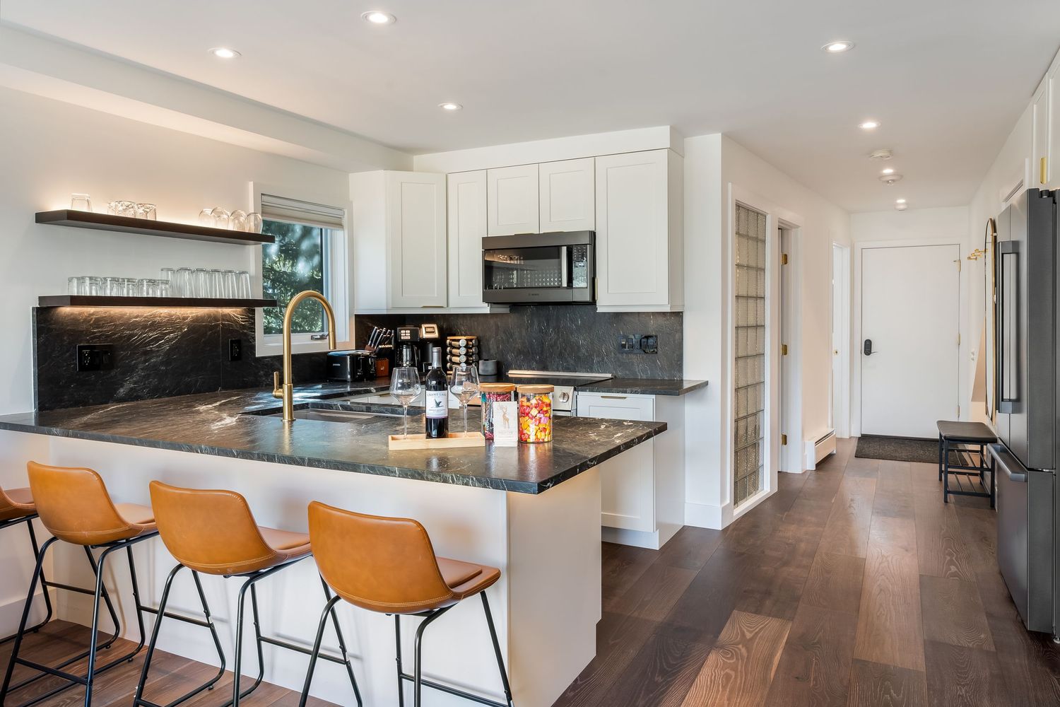 Sleek modern kitchen with dark marble countertops, white cabinets, and leather bar stools at island.