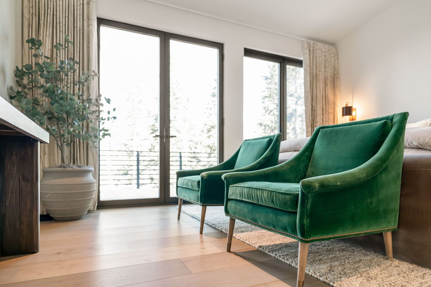 Modern living room with emerald green velvet armchairs, large windows, and contemporary decor accents.