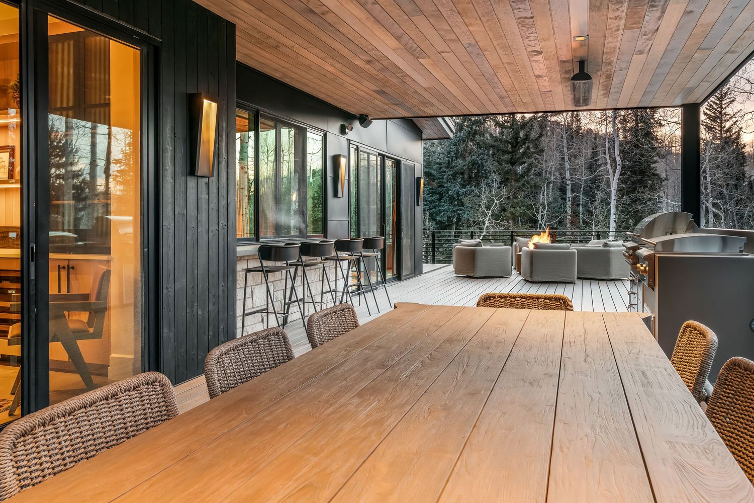 Contemporary wooden deck extends along glass-walled exterior with outdoor seating and forest views.