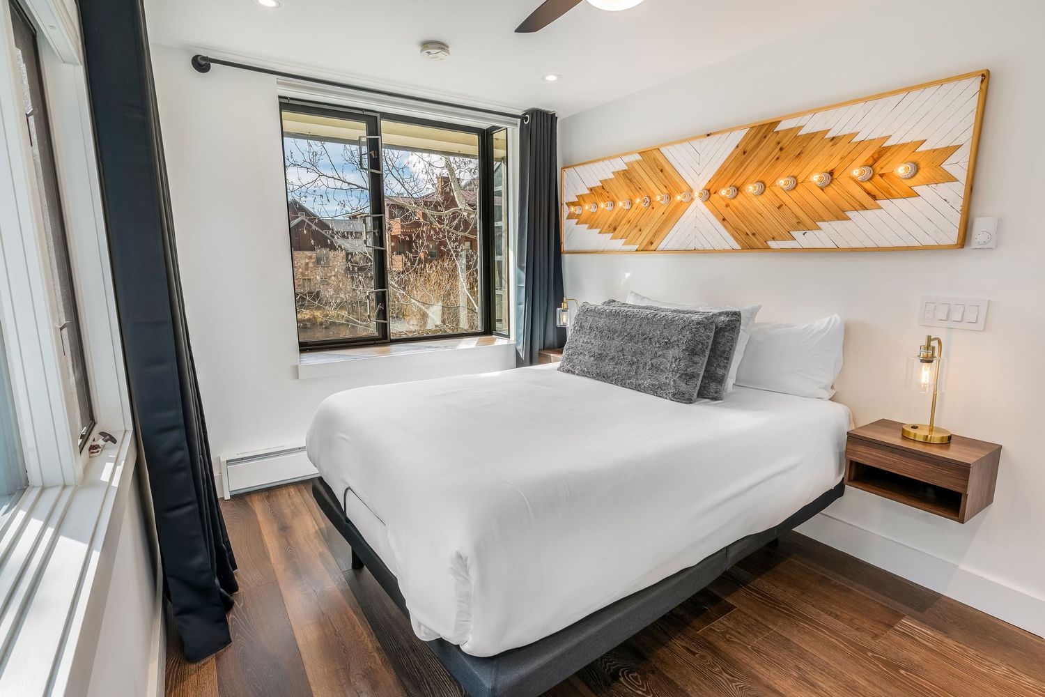 Modern bedroom with white bedding, wood floors, large window, and decorative golden leaf wall art above the bed.