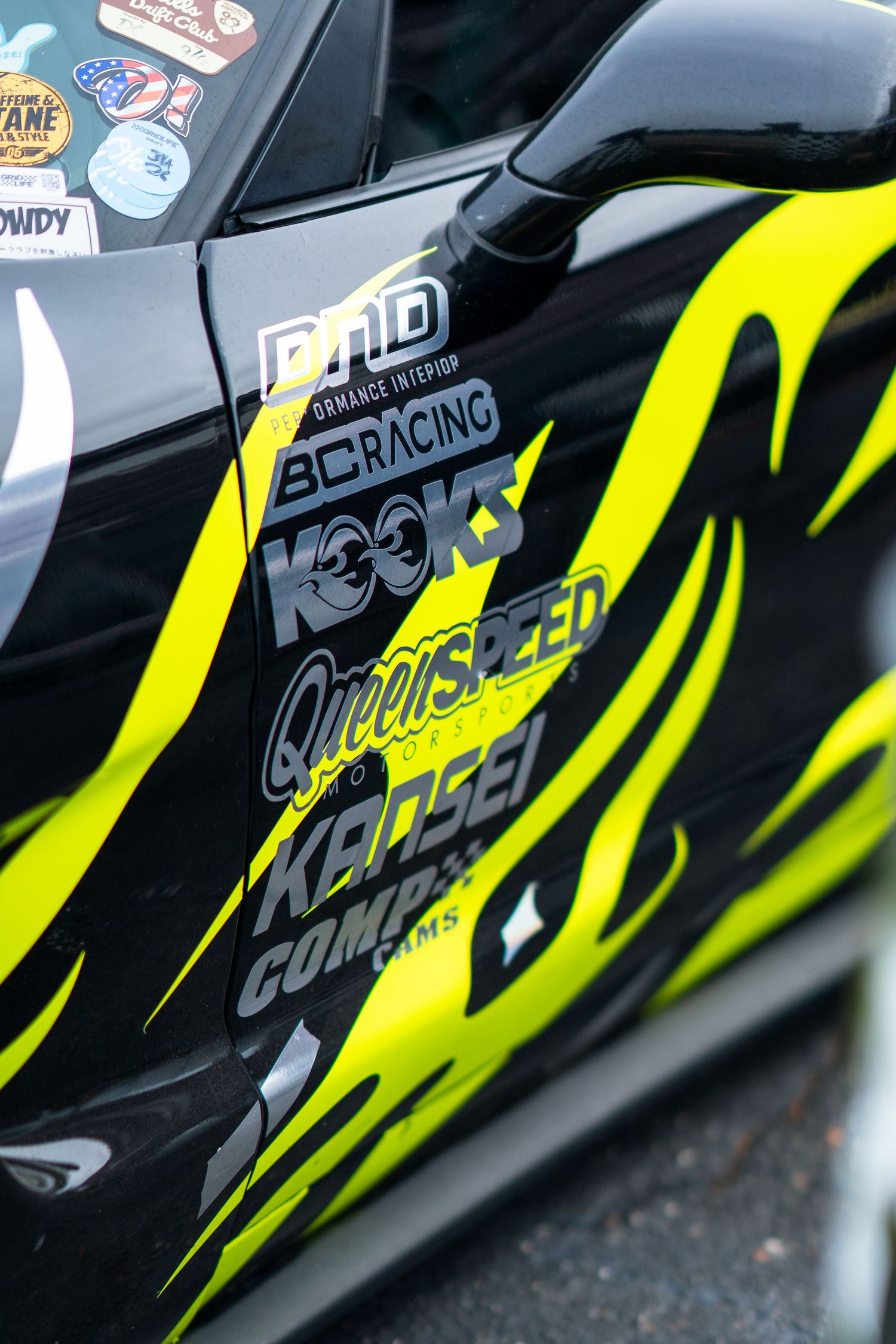 Black race car door with neon yellow flame graphics and multiple sponsor decals including BC Racing and Kooks.