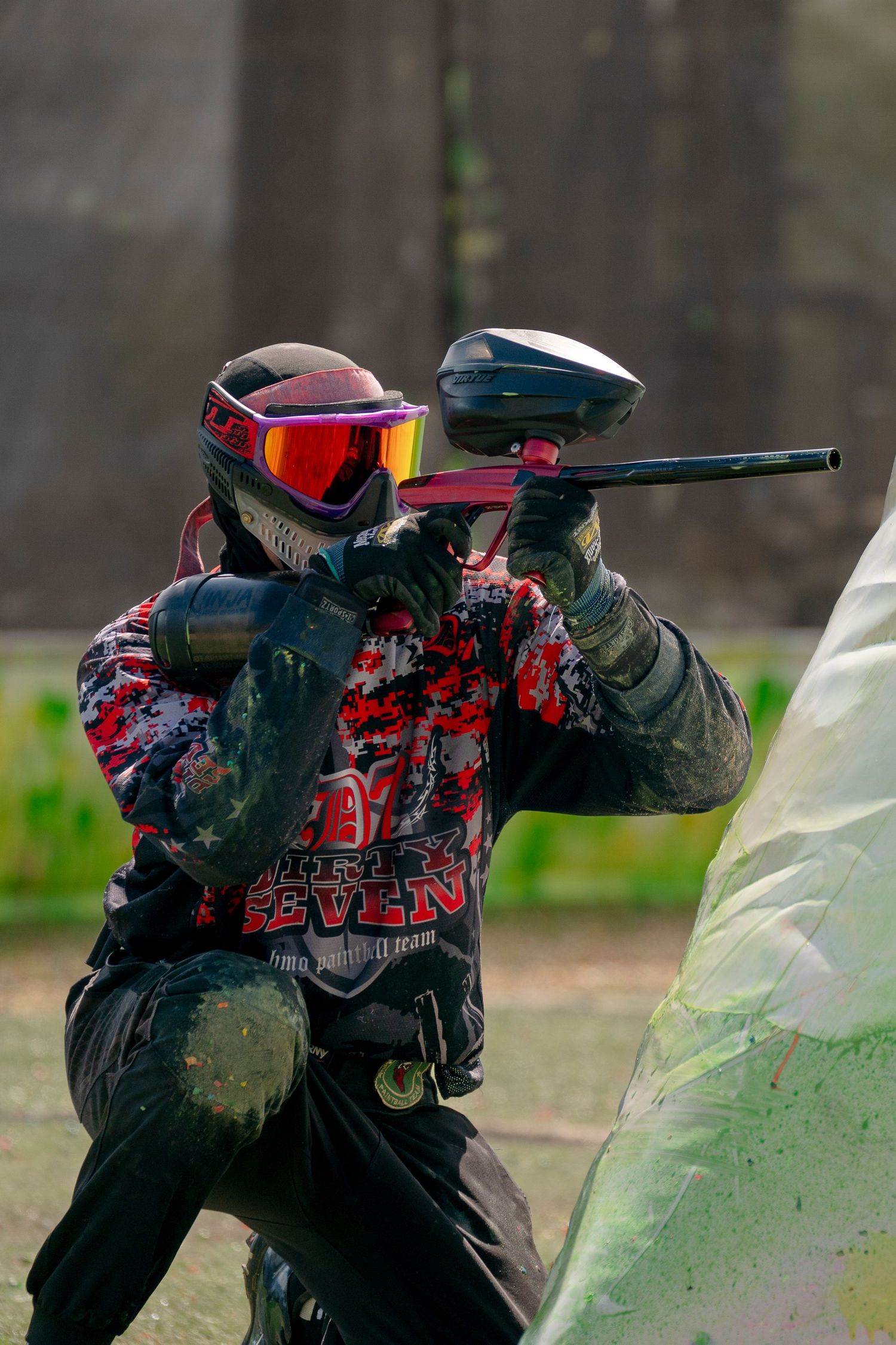 Paintball player in protective gear aims marker gun during intense gameplay.