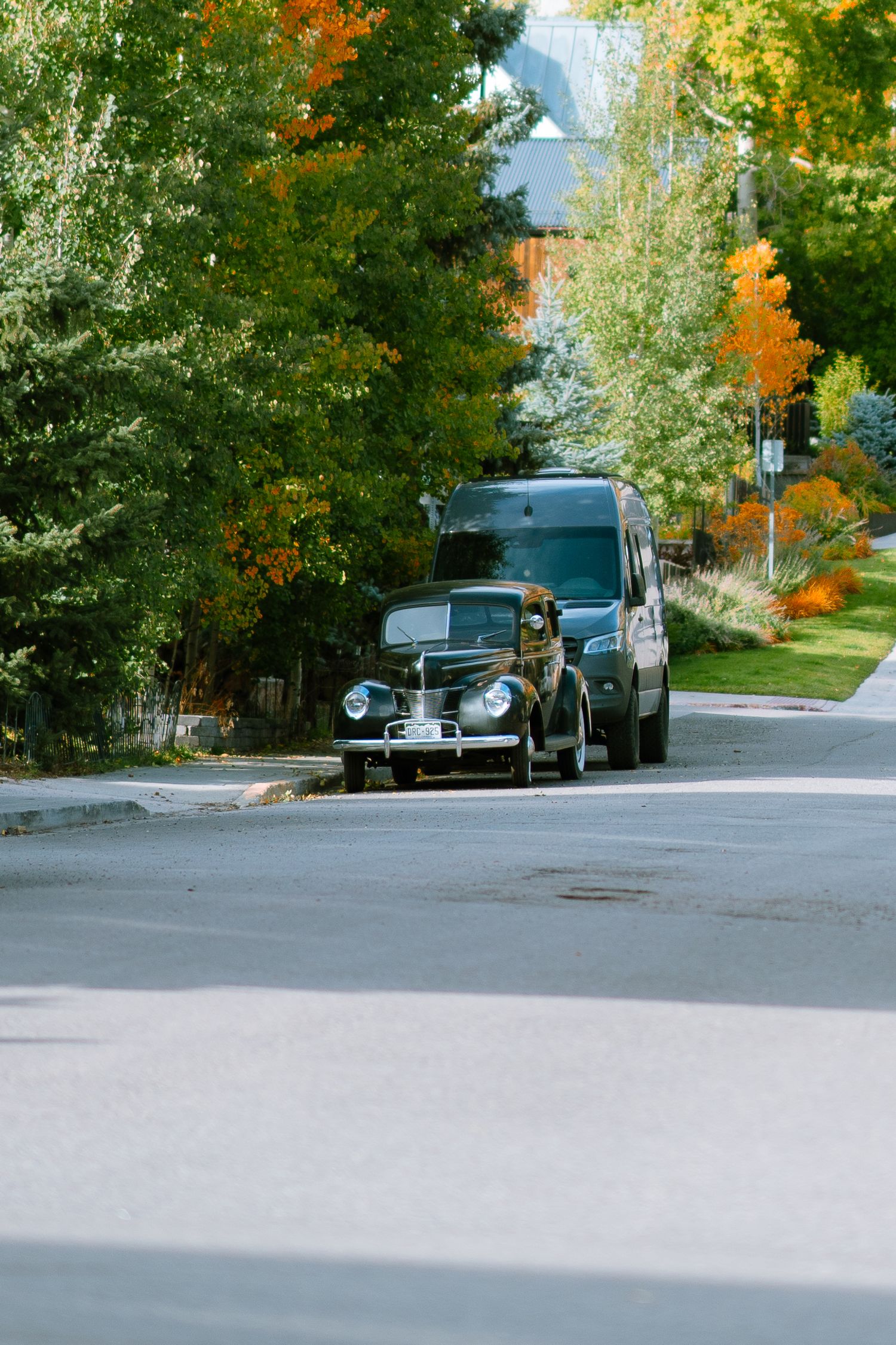 Classic vintage car parked on a tree-lined autumn street with colorful fall foliage.