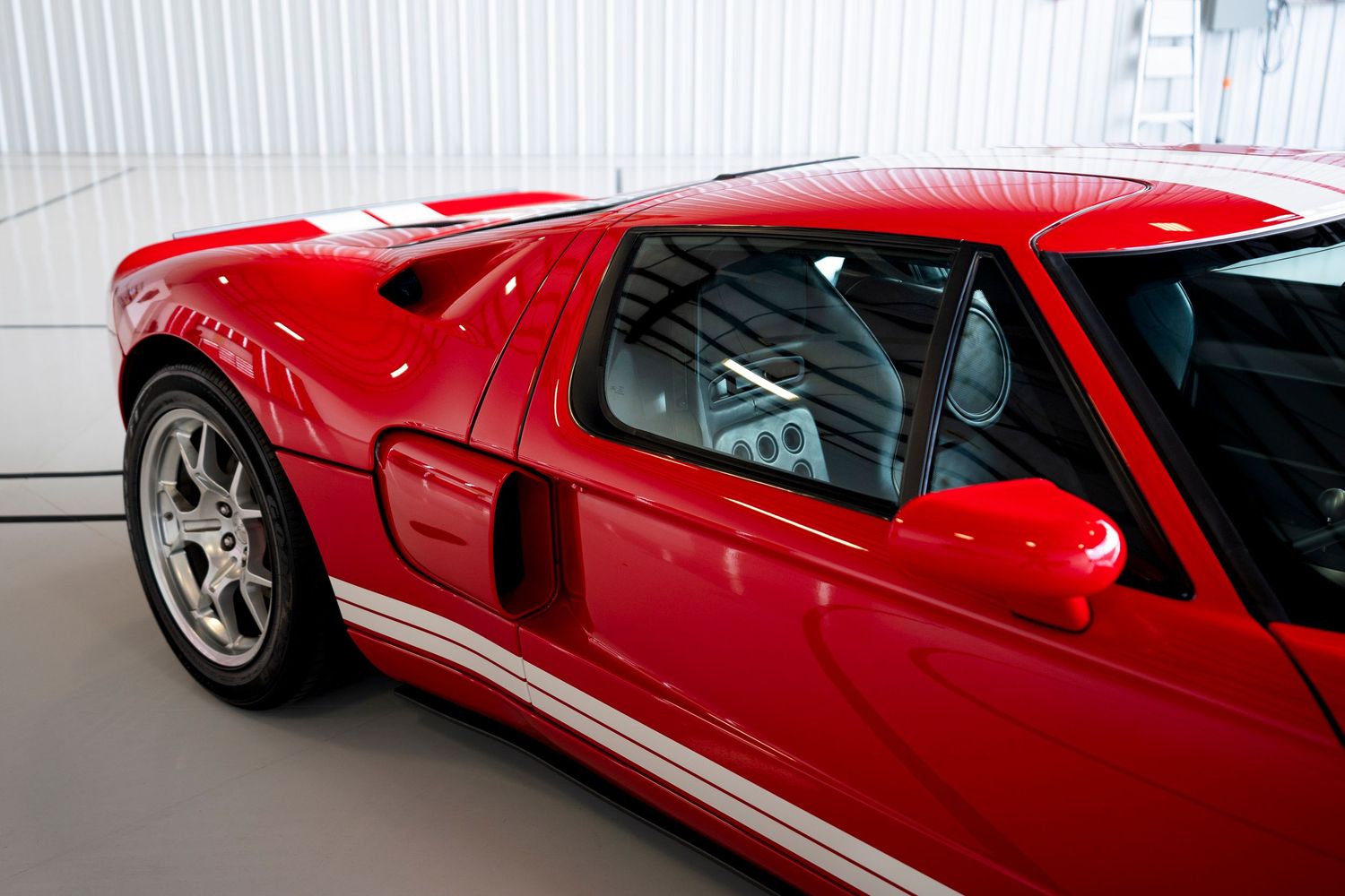 Side profile of a red performance car with white racing stripes in a showroom.