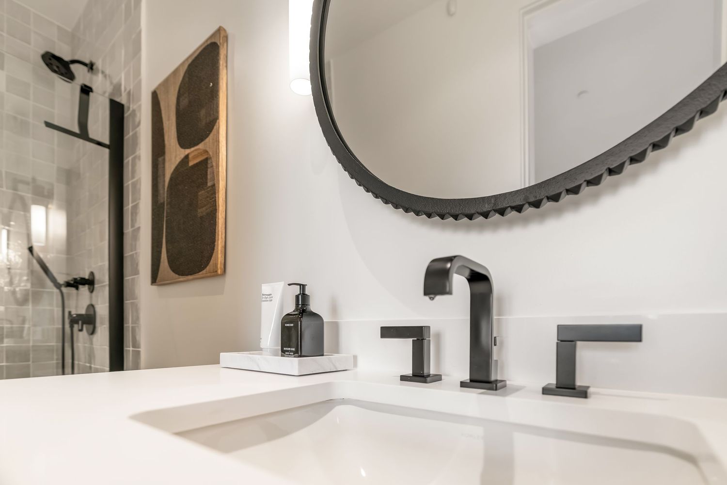 Modern bathroom interior with white marble vanity, matte black fixtures, and round mirror mounted on white wall.