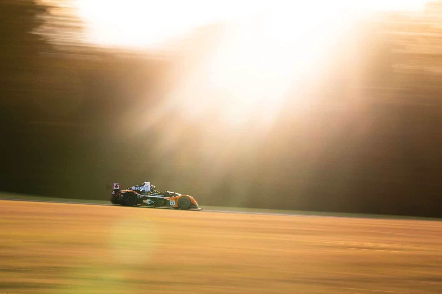 Race car speeds past during golden sunset creating dramatic lighting on the track.