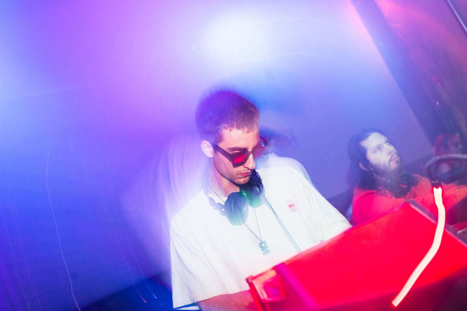 DJ performing at a nightclub with vibrant purple and blue lighting effects creating an energetic atmosphere.