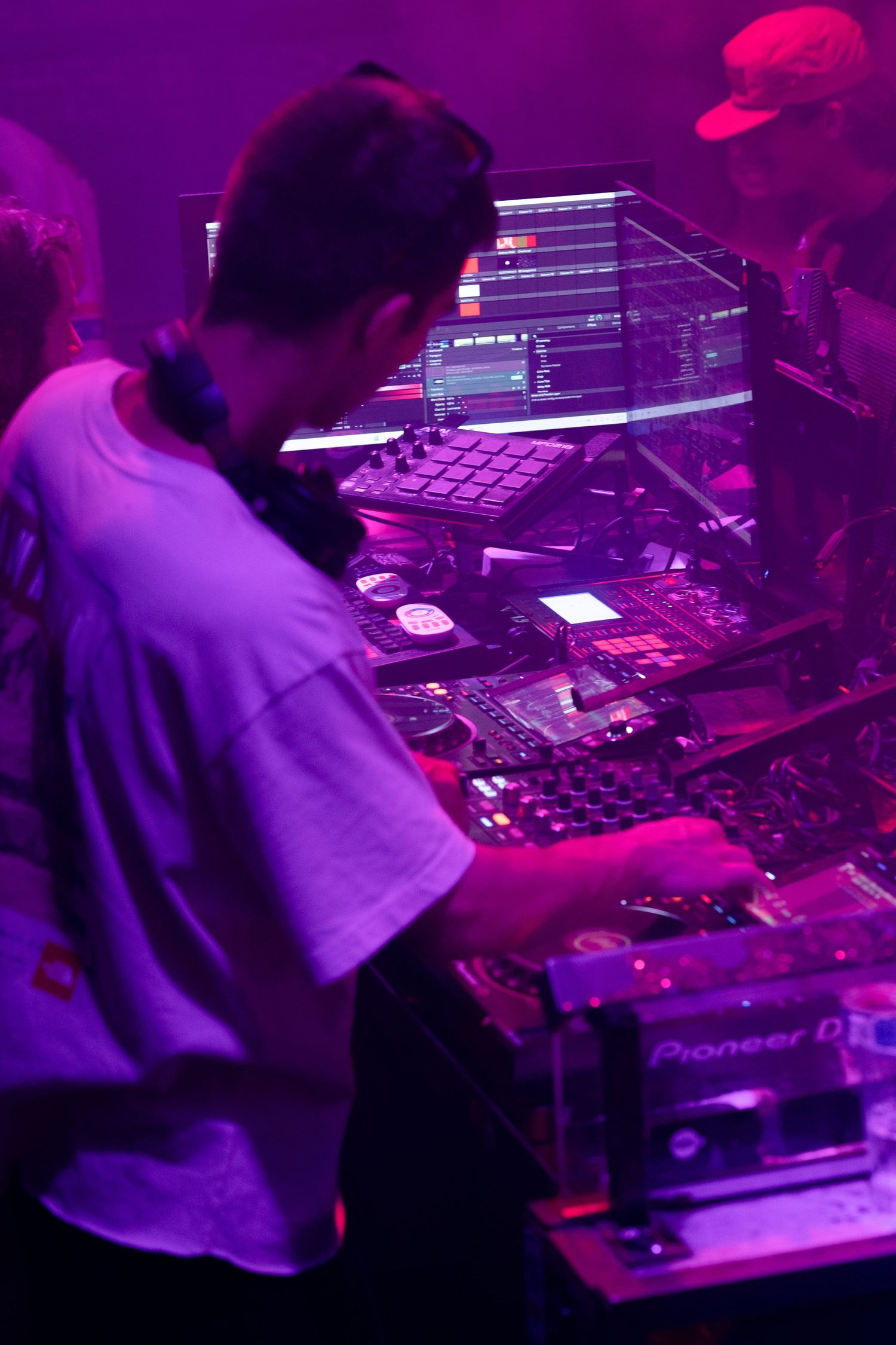 DJ works on Pioneer equipment bathed in purple lighting at a nightclub performance.