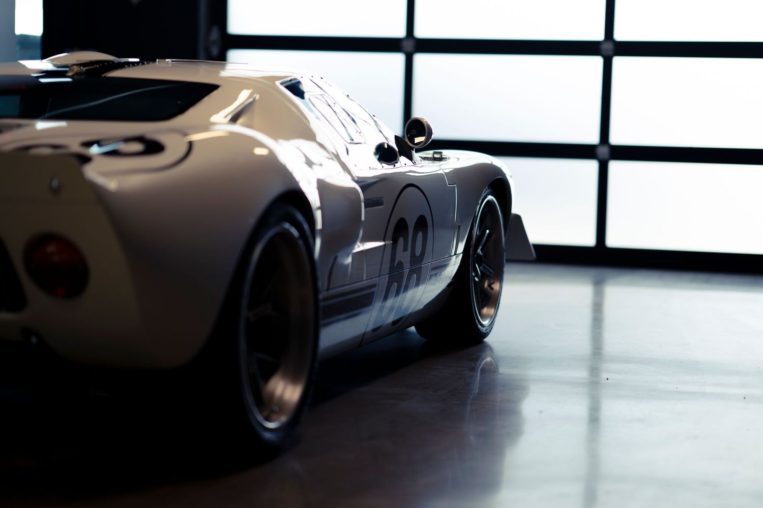 Classic white race car photographed from multiple angles in a modern showroom with large windows.