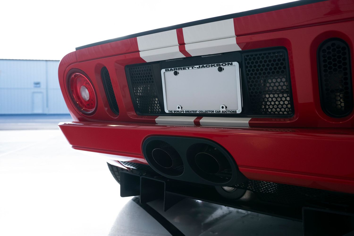 Close-up of red sports car rear bumper with dual exhaust and license plate mount.