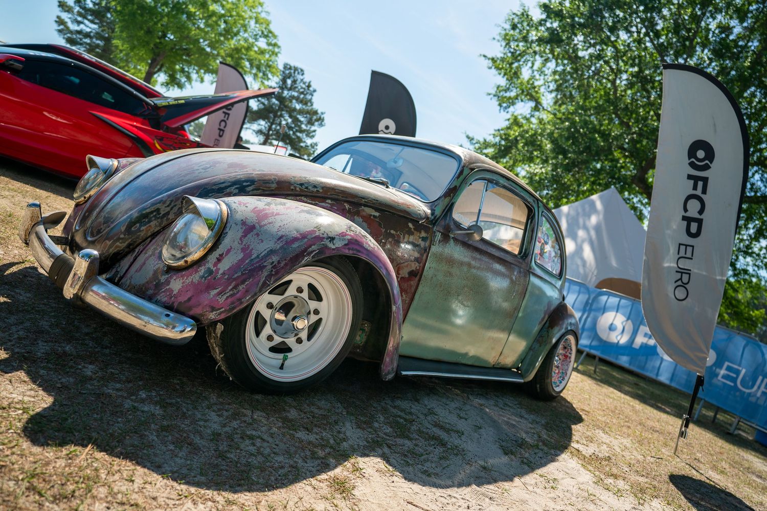 Custom painted vintage VW Beetle with lowered stance displayed at outdoor car show.