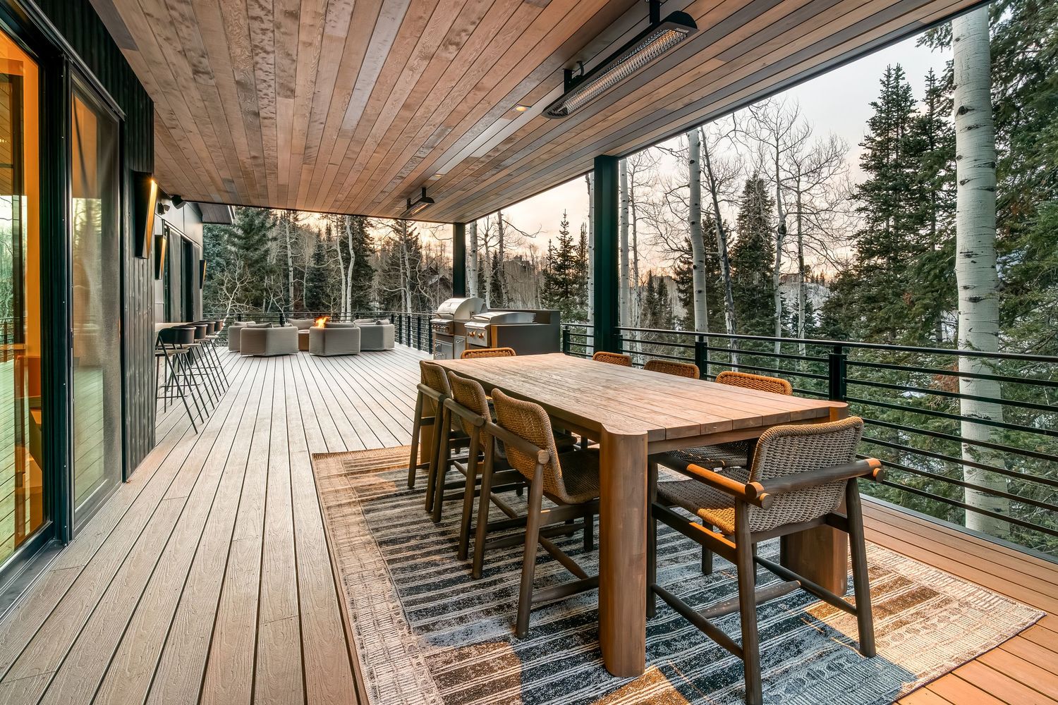 Expansive wooden deck with glass barriers extending along modern mountain home with scenic forest views.