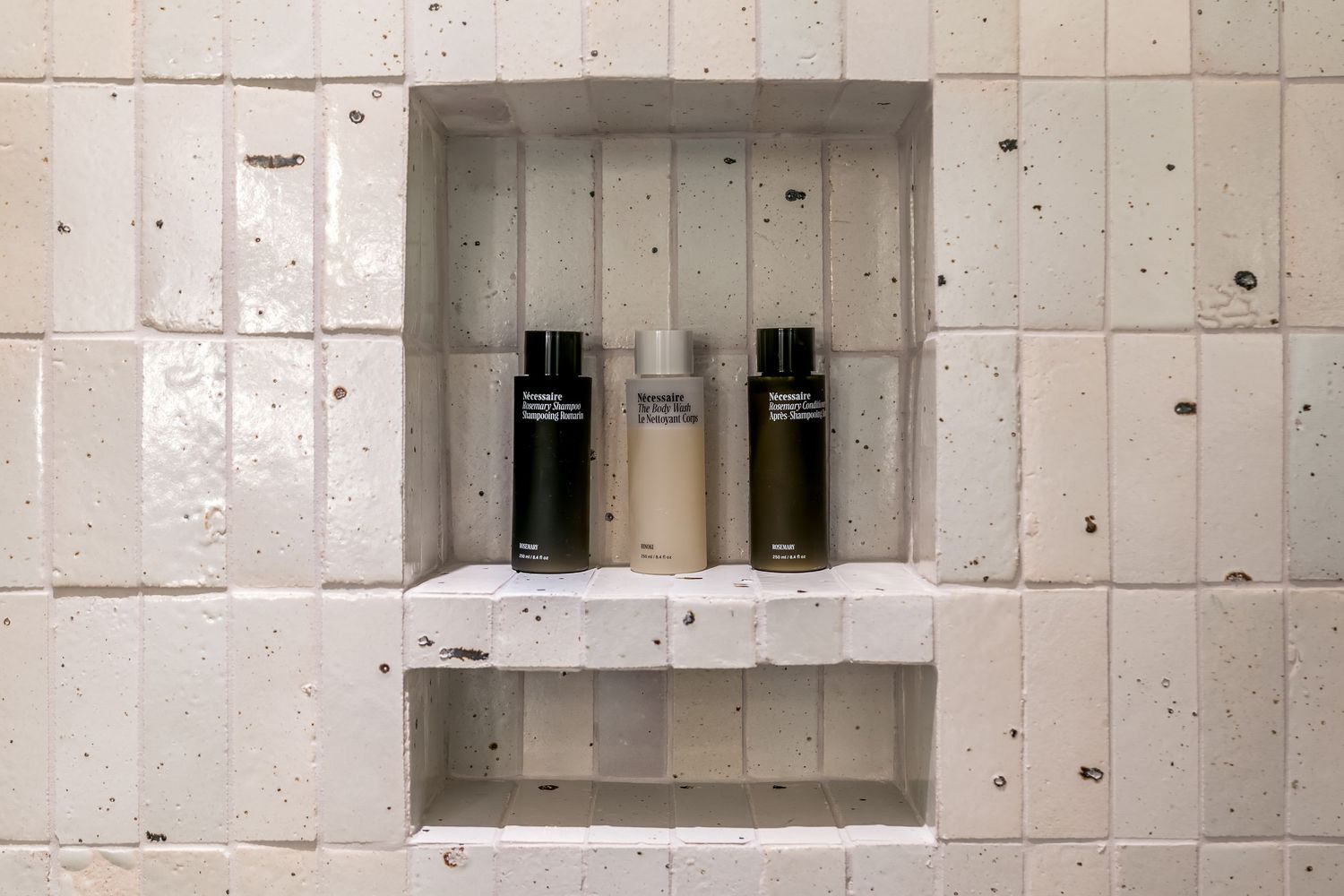 Concrete wall with recessed shelving niches displaying bathroom products in a modern spa-like setting.