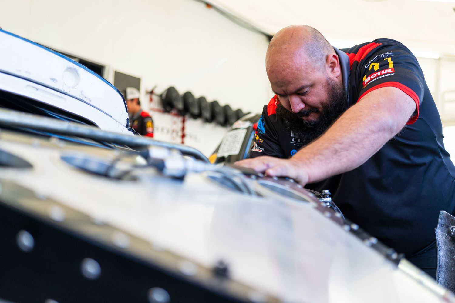 Race car mechanic making adjustments and inspections under the vehicle during maintenance.