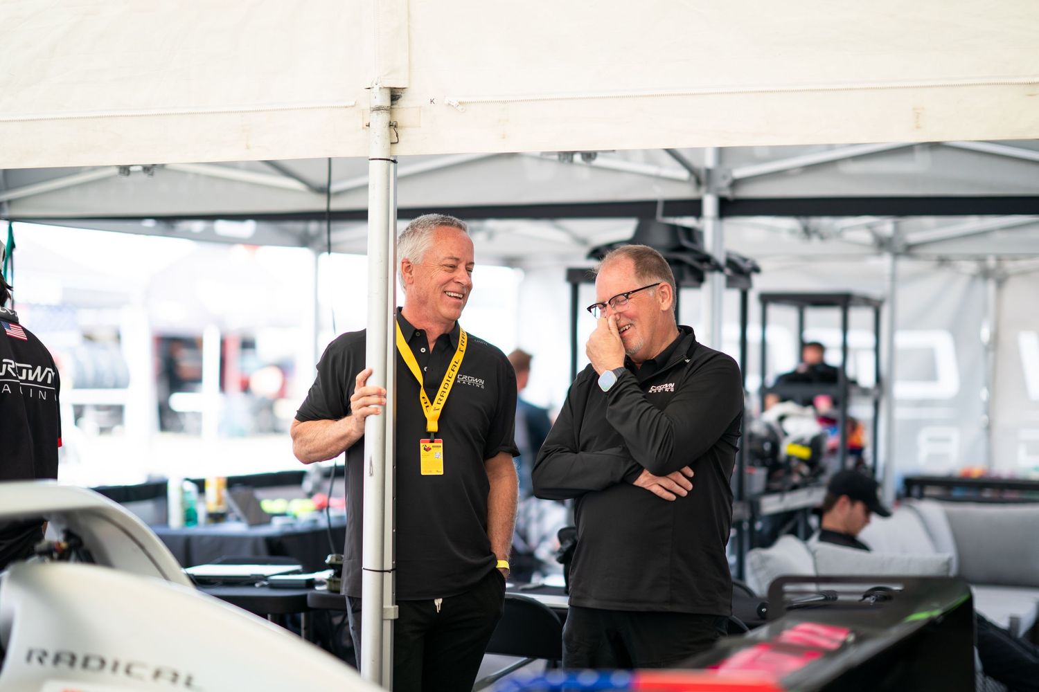 Racing team personnel working on equipment and data analysis in the garage area.