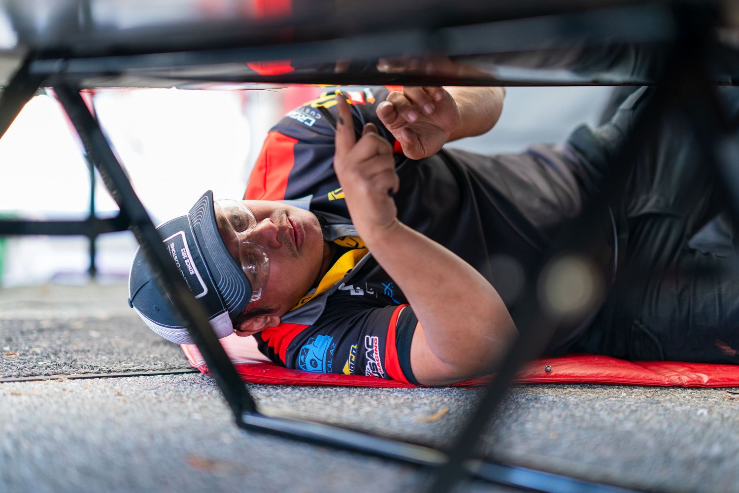 Technician performing underbody maintenance on a professional racing vehicle.