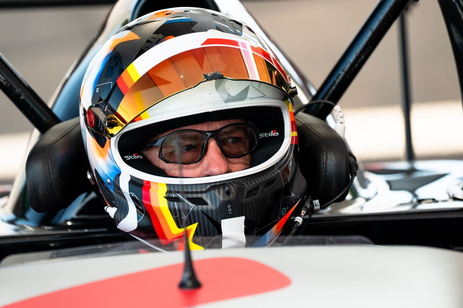 Driver wearing racing helmet sits in cockpit of Formula 1 car during pre-race preparations.
