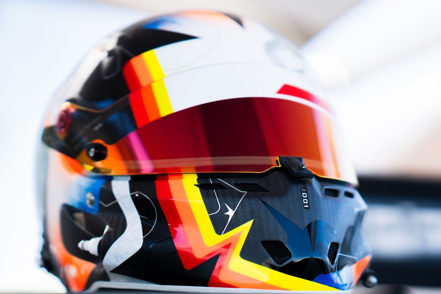 Close-up view of a racing helmet with orange and blue accents against a blurred background.