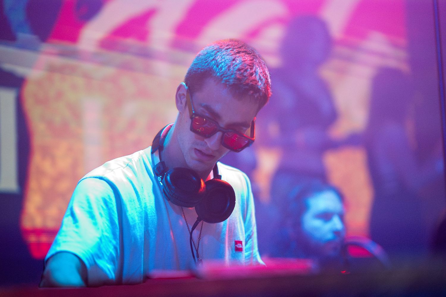 DJ performing at a nightclub bathed in vibrant blue and purple lighting during an electronic music event.