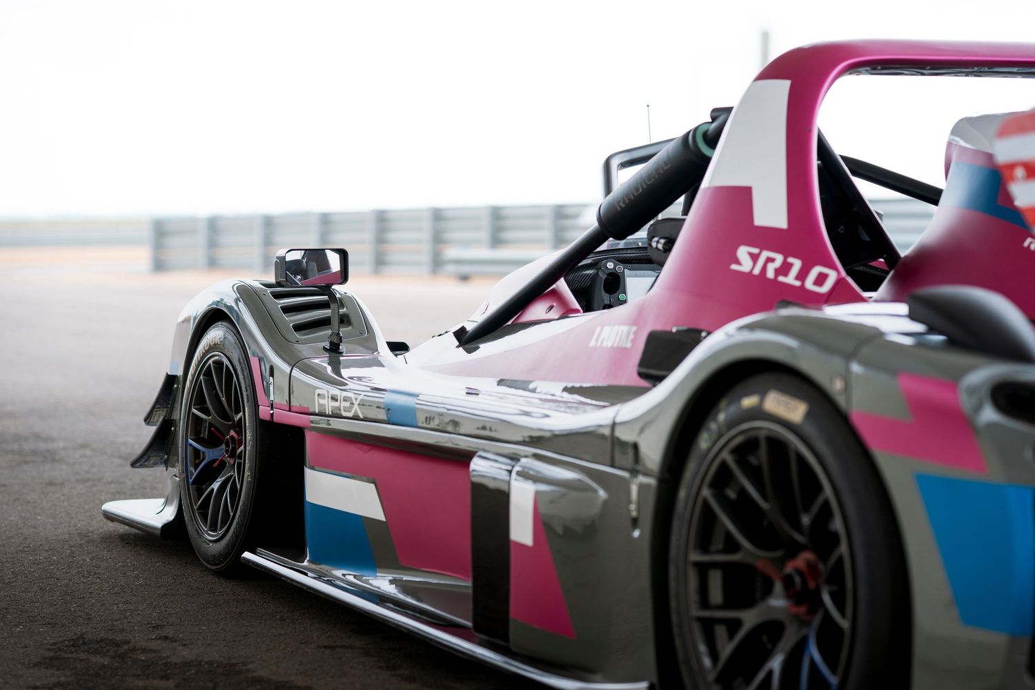 Pink and blue racing car with aerodynamic bodywork and large rear wing on a racetrack.