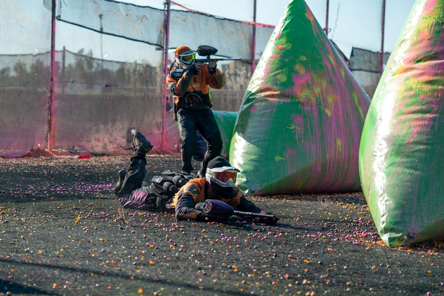 Paintball players taking cover behind green inflatable bunkers during an outdoor competitive paintball game.