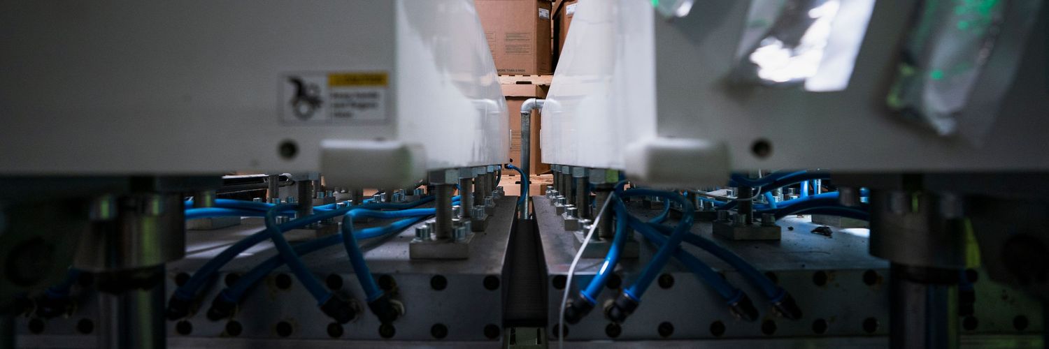 Dark industrial manufacturing space with machinery silhouettes and ambient lighting.