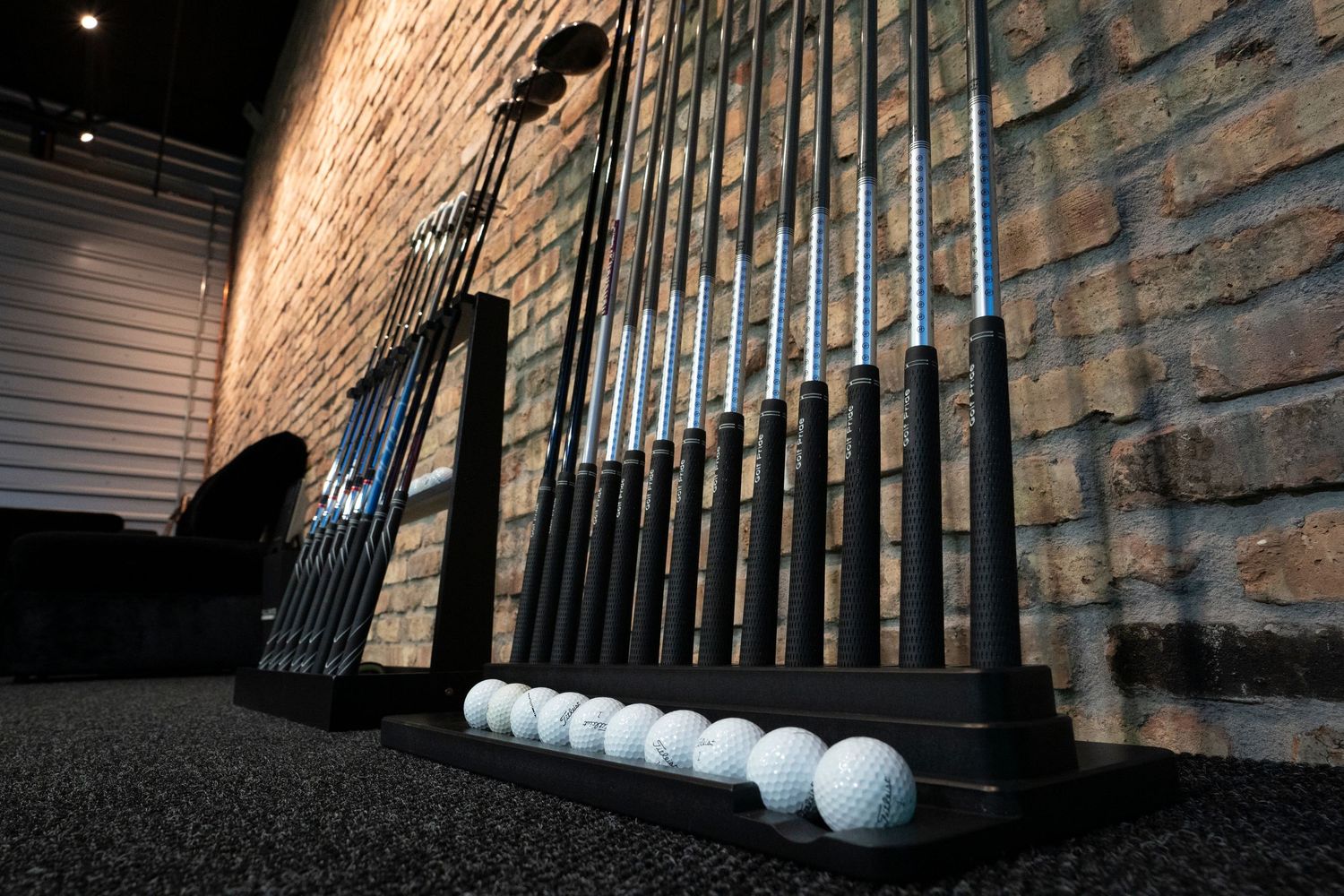 Row of golf clubs displayed against textured stone wall with dramatic lighting.