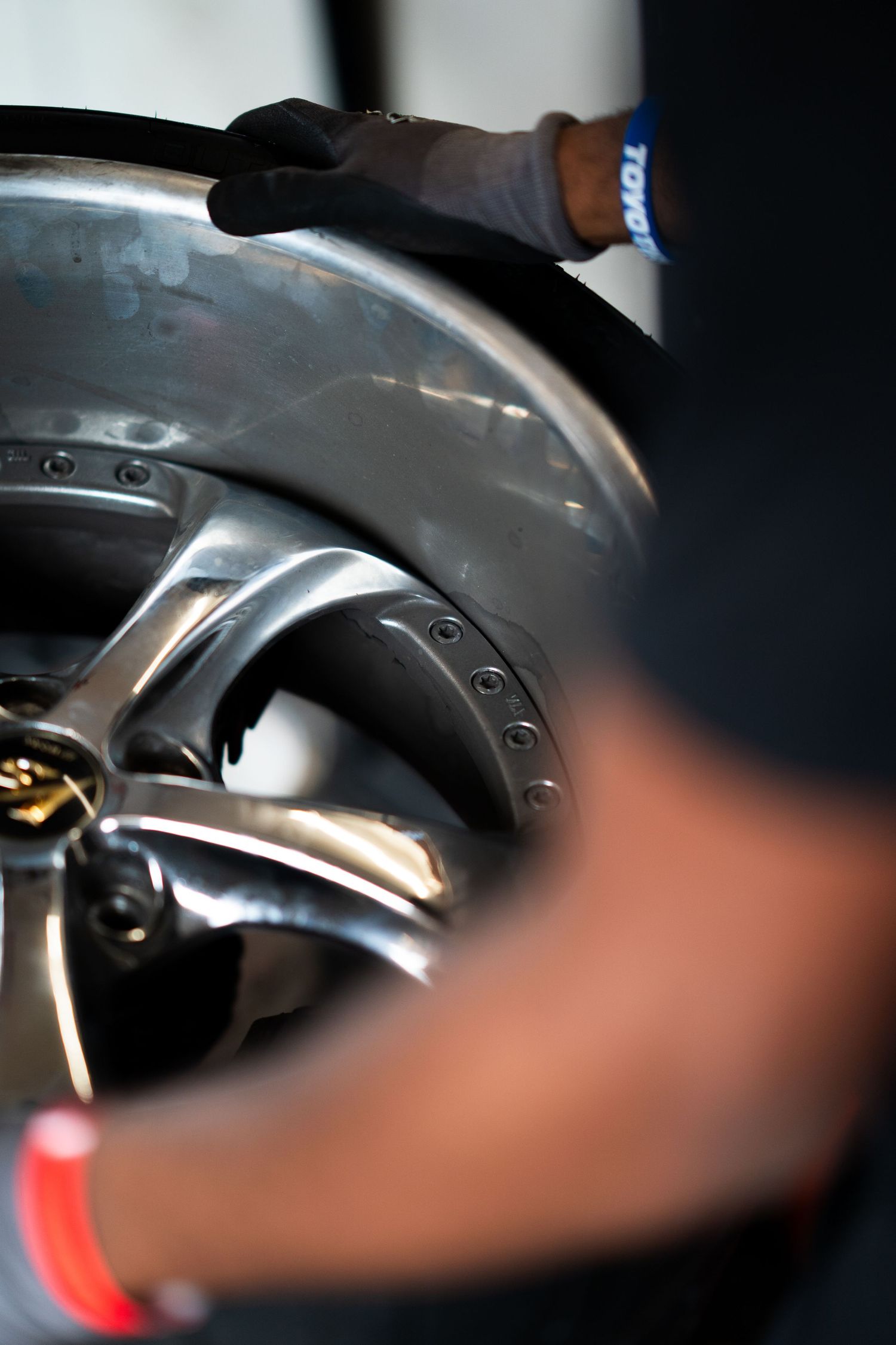 Mechanic in black gloves handling a polished racing wheel rim during a pit stop preparation.