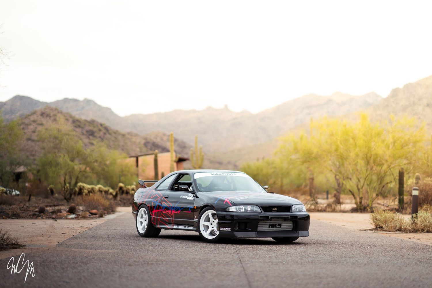 A sleek black Nissan Skyline R32 GT-R sports car parked in a desert landscape during golden hour.