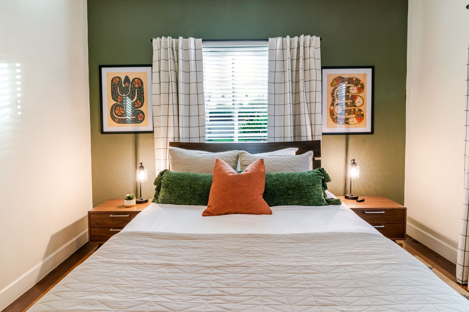Contemporary bedroom with dark green accent wall, white bedding, and framed artwork.