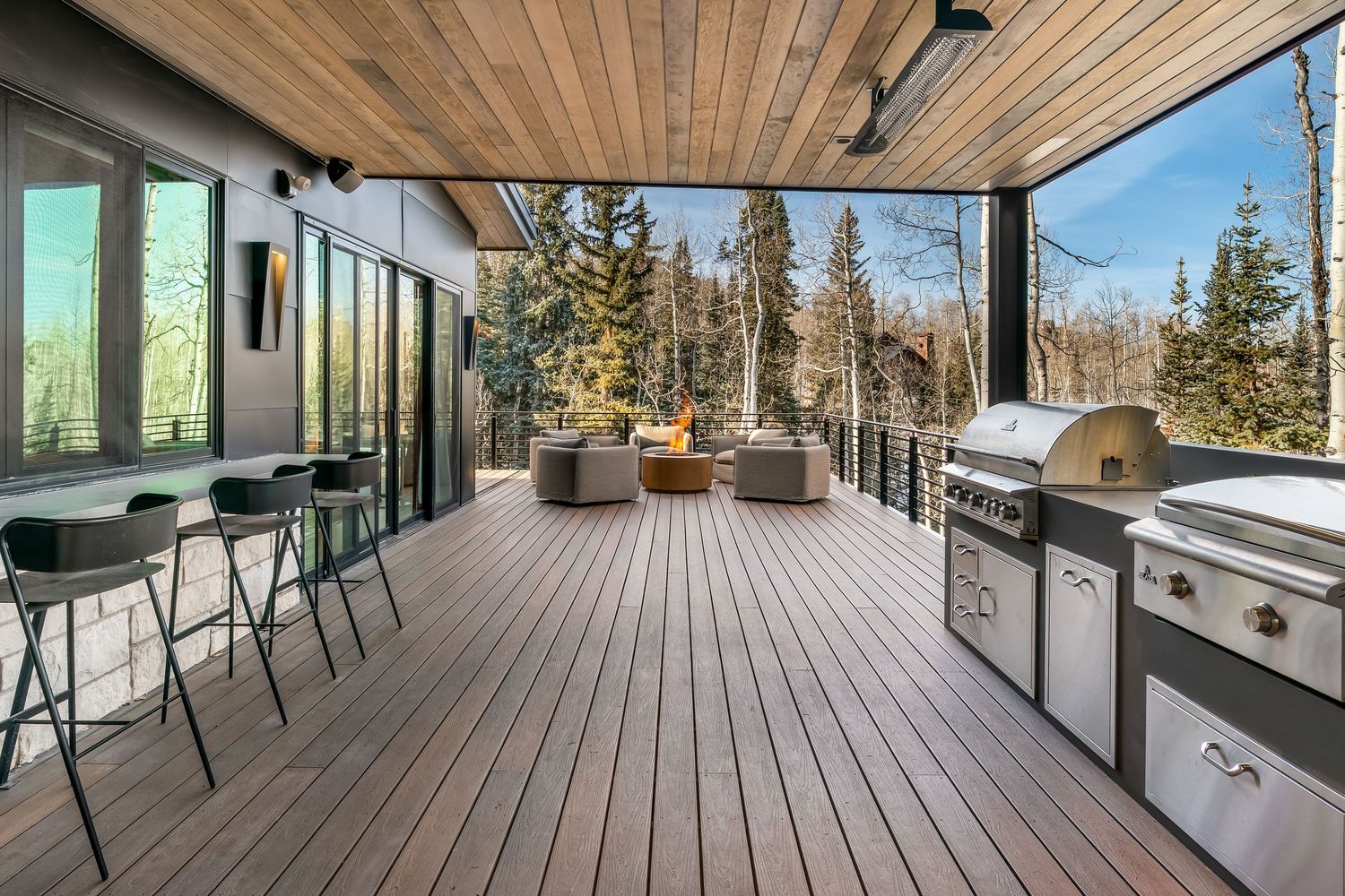 Expansive wooden deck with panoramic mountain views and glass railing system stretching along the exterior.
