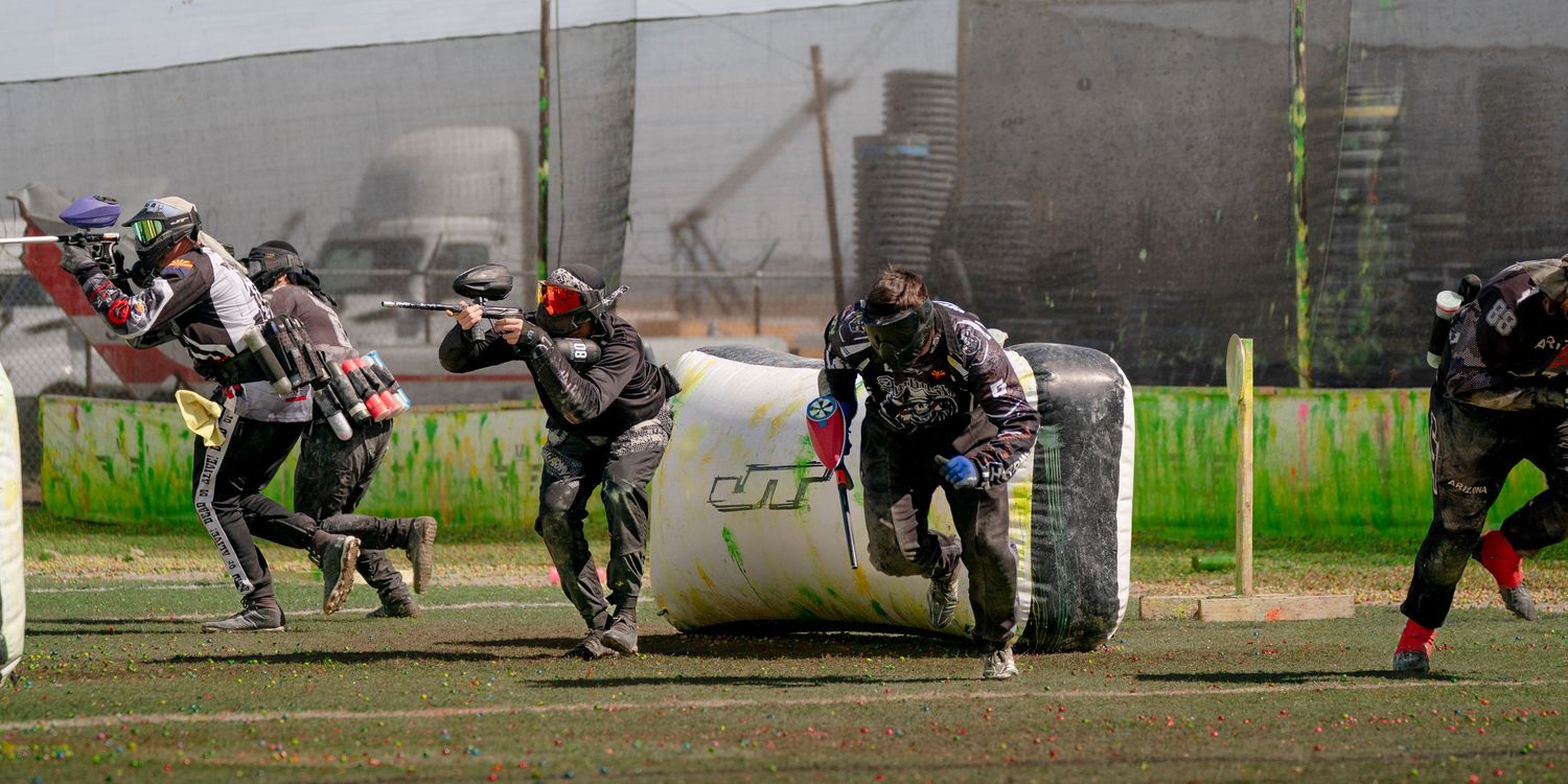 Multiple paintball players crouching behind barriers in formation during a competitive game.