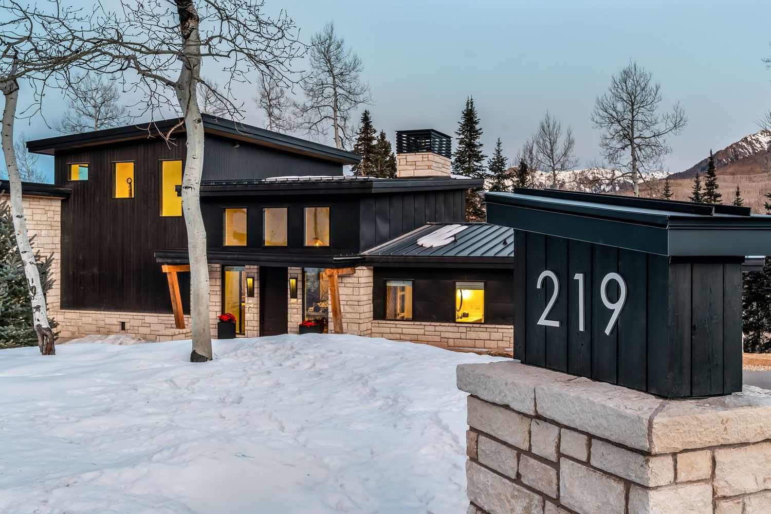 Modern black and white cabin architecture with illuminated windows glows against a snowy winter forest backdrop.