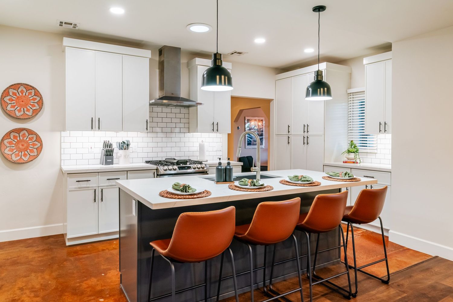 Sleek kitchen island with orange bar stools and modern pendant lights in an open-concept space.