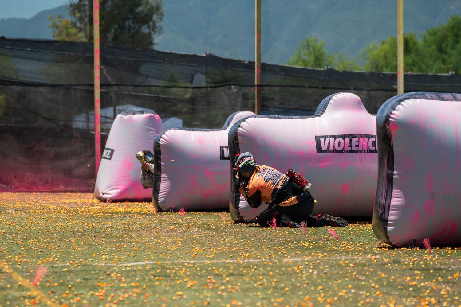 Paintball player crouching behind pink inflatable bunkers labeled Violence during outdoor tournament match.