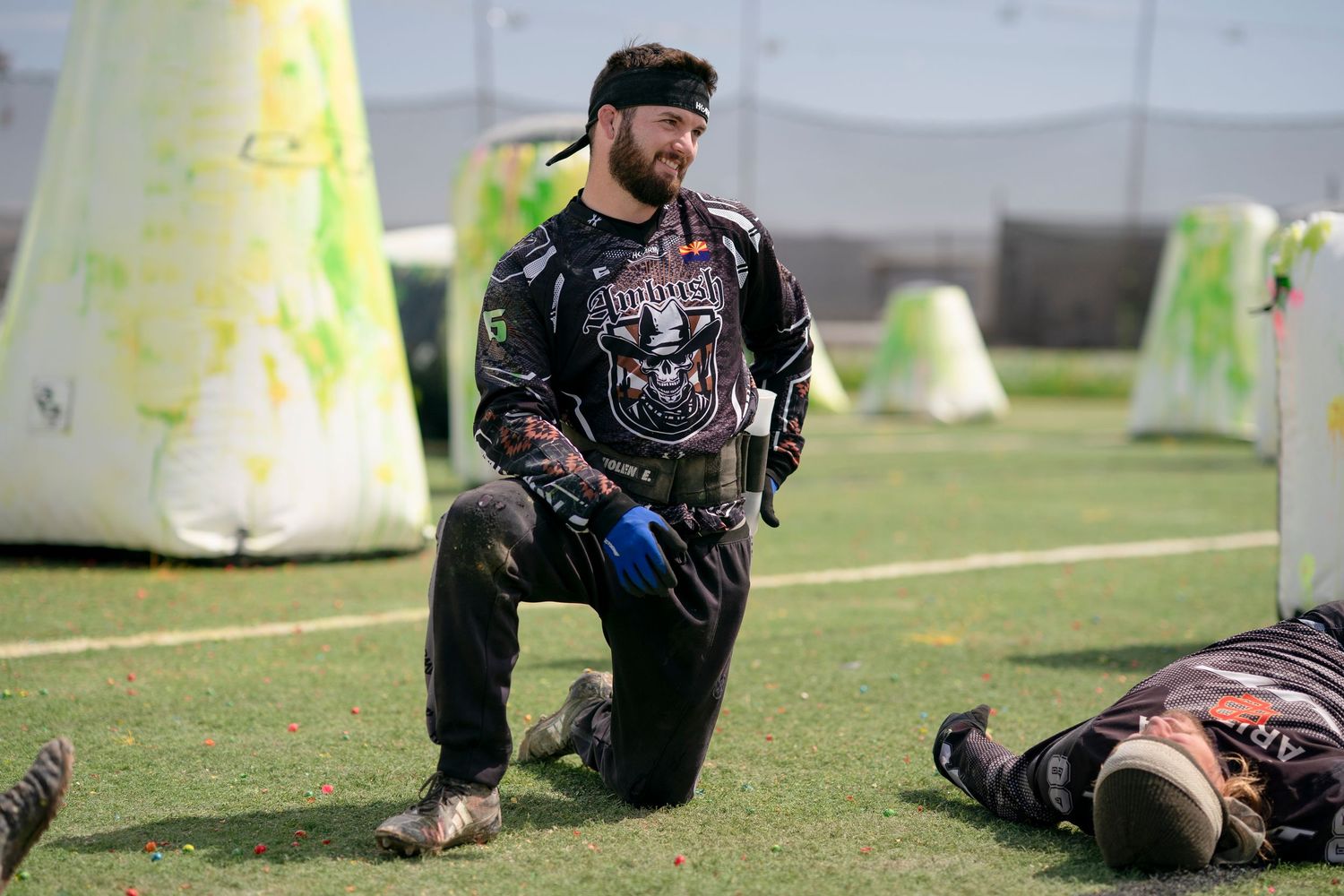 Paintball player in tactical gear kneeling behind yellow bunker during competitive match.