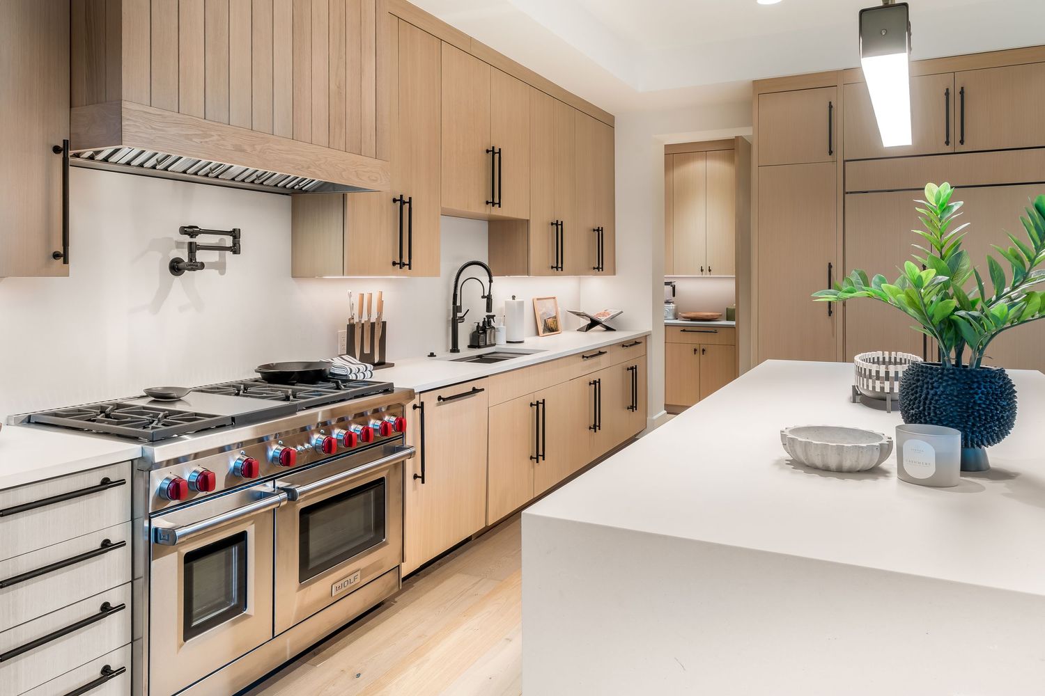 Modern kitchen design features sleek wood cabinets, white countertops, and stainless steel appliances in an open layout.
