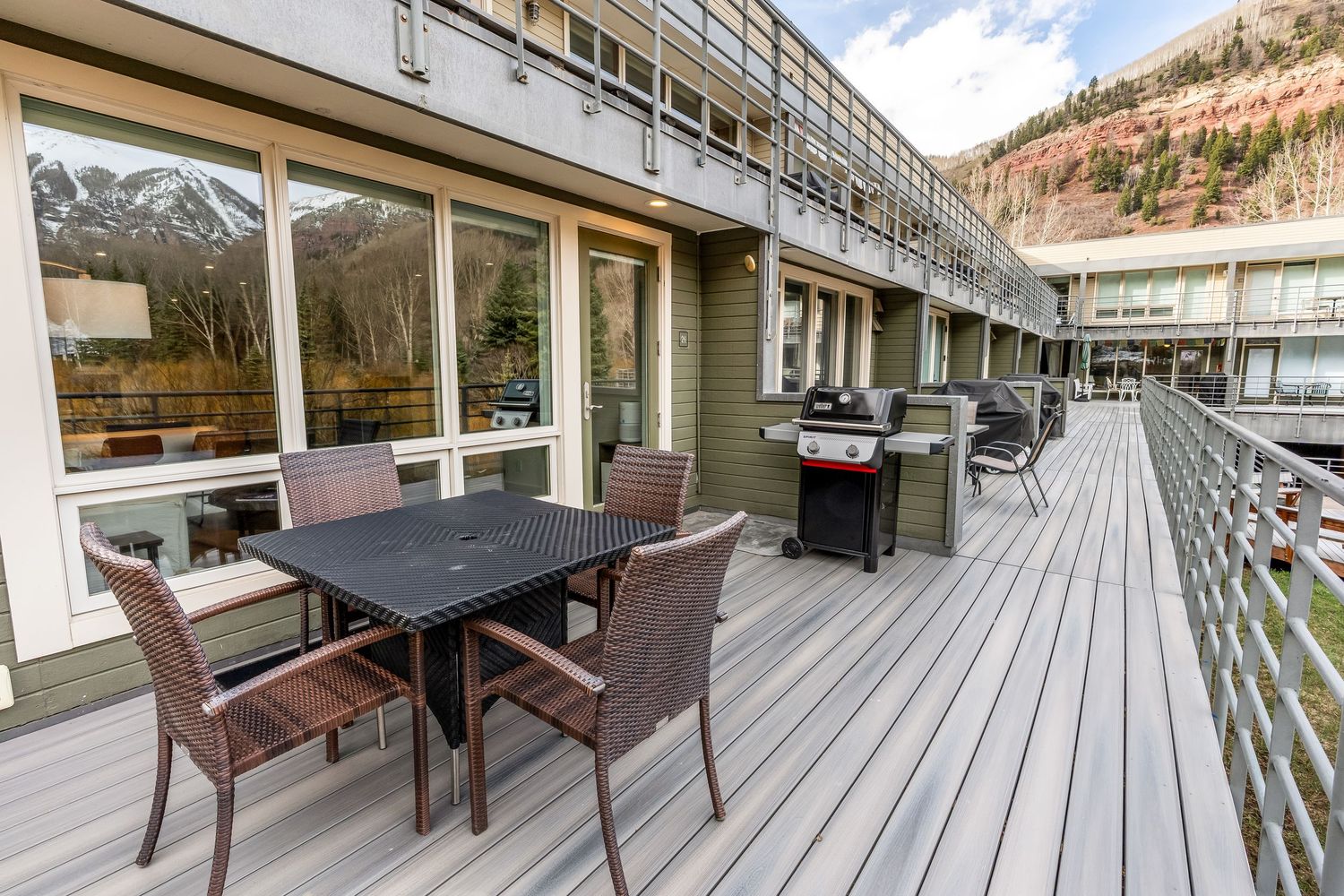Spacious wooden deck with outdoor dining set and gas grill, overlooking mountain views at a multi-story building.