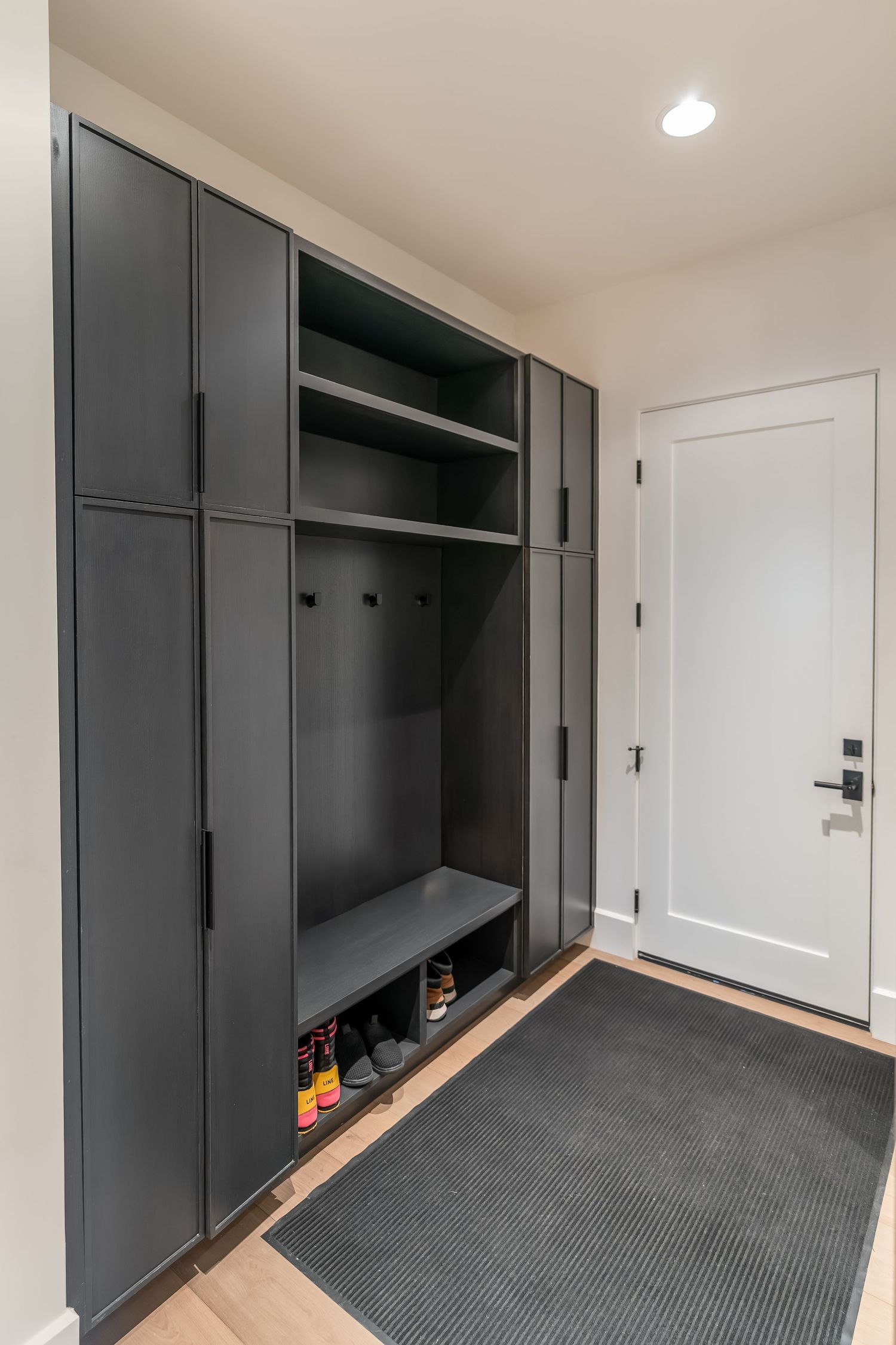 Modern mudroom with black built-in storage cabinets and a gray entry mat near white door.